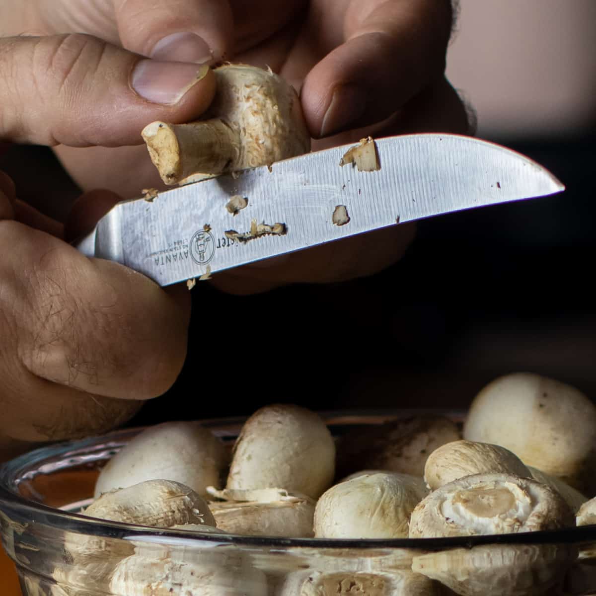 A close up picture of a mushroom step being cut off with a sharp knife.