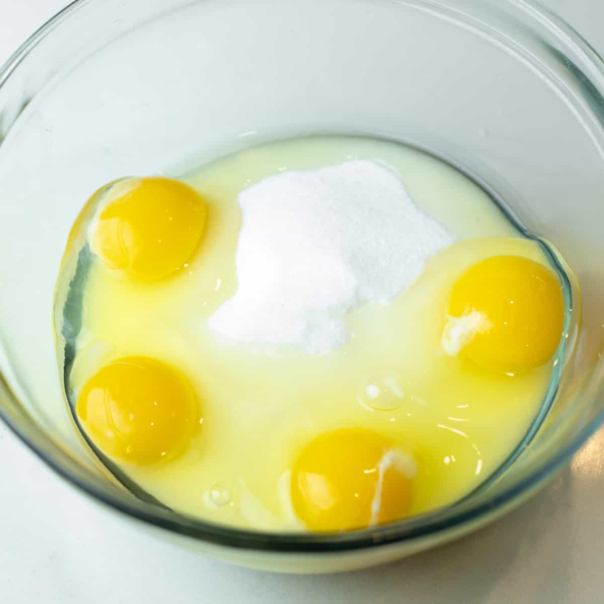 Four eggs in a glass bowl with sugar.